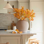 A large round beige vase filled with autumn florals