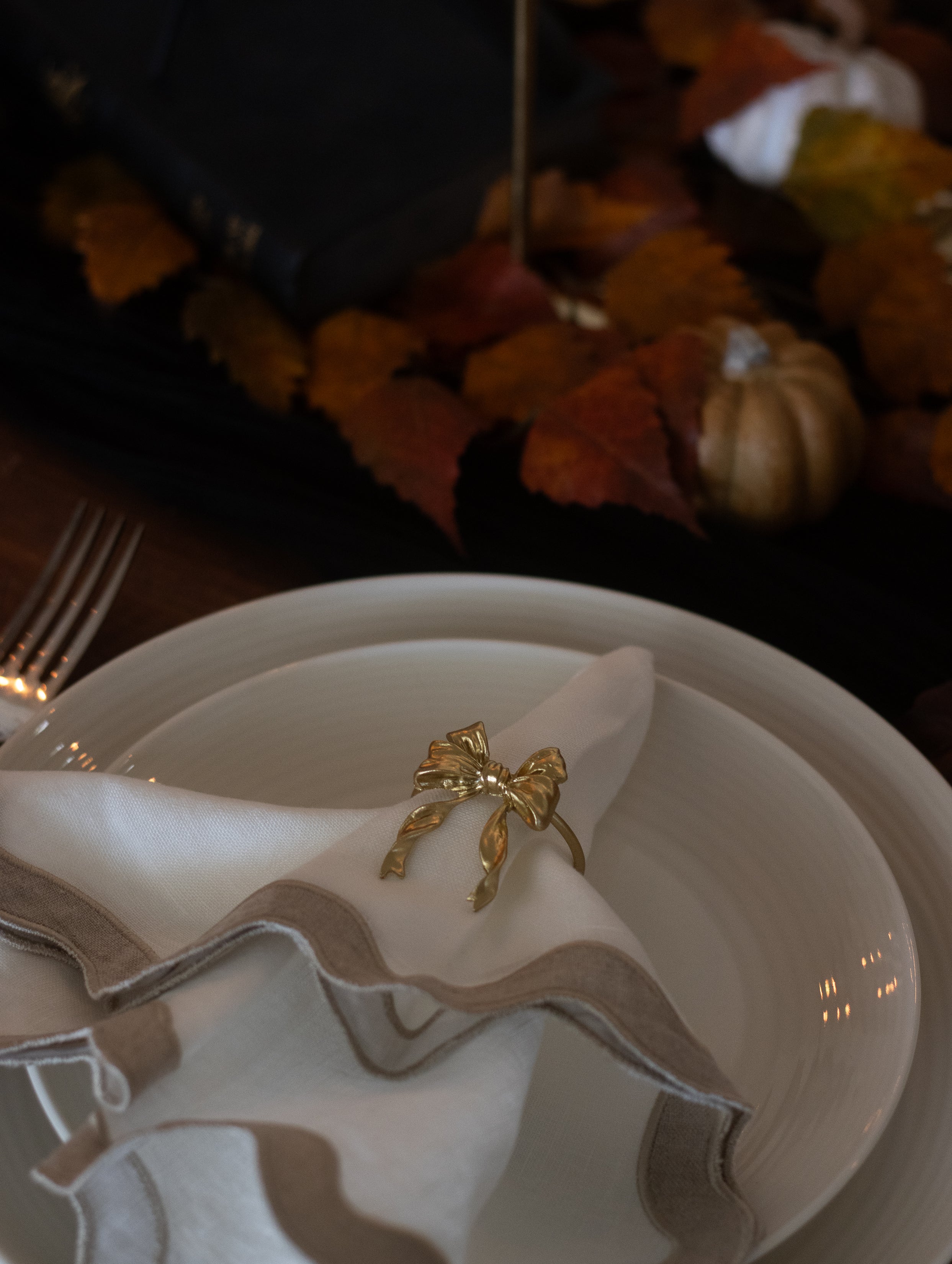 Gold bow napkin ring on a white plate with fall leaves and pumpkins in the background