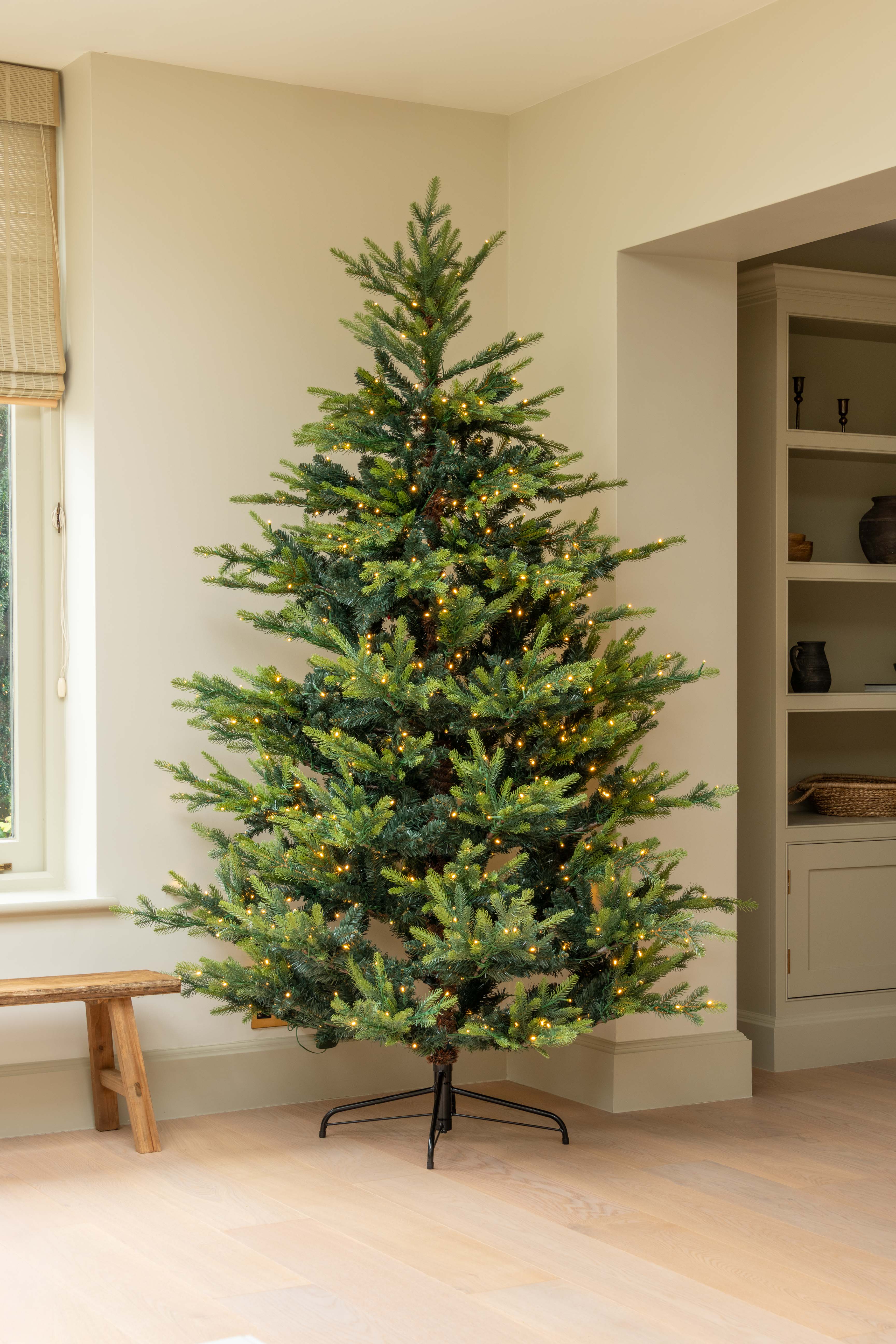 Decorated Christmas tree in a room with a window and shelves.