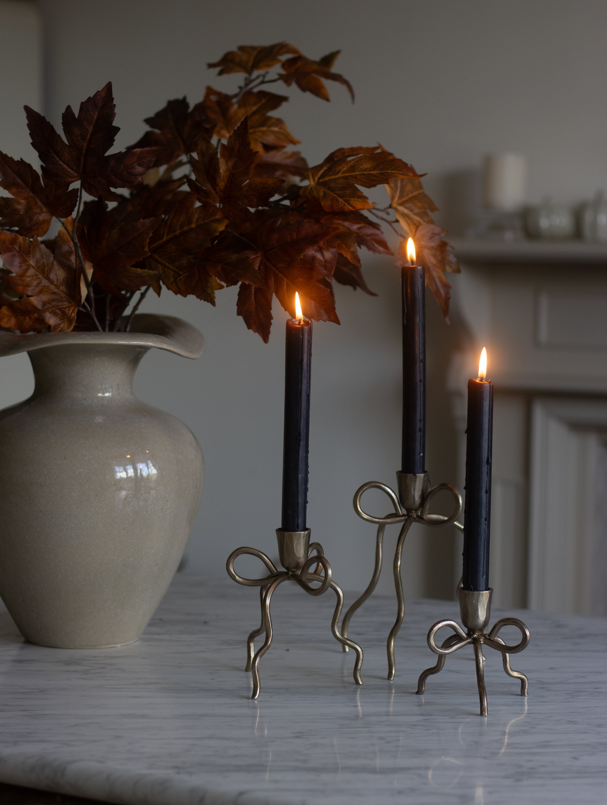 Decorative candle holders with lit candles next to a vase on a marble surface.