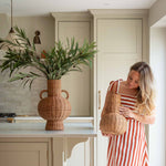 Handwoven with care and tradition, the Alderfield Jug brings the charm of rustic craftsmanship into your space. Inspired by heritage vessels once used to gather spring water or display wild blooms, this piece features a rounded base, tall neck, and two looped handles for a timeless silhouette. Made from natural rattan, its warm, earthy tones and intricate weave tell a story of simple living and enduring beauty. Whether placed on a farmhouse table or nestled in a sunlit corner, the Alderfield Jug adds textur