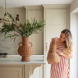 Handwoven with care and tradition, the Alderfield Jug brings the charm of rustic craftsmanship into your space. Inspired by heritage vessels once used to gather spring water or display wild blooms, this piece features a rounded base, tall neck, and two looped handles for a timeless silhouette. Made from natural rattan, its warm, earthy tones and intricate weave tell a story of simple living and enduring beauty. Whether placed on a farmhouse table or nestled in a sunlit corner, the Alderfield Jug adds textur