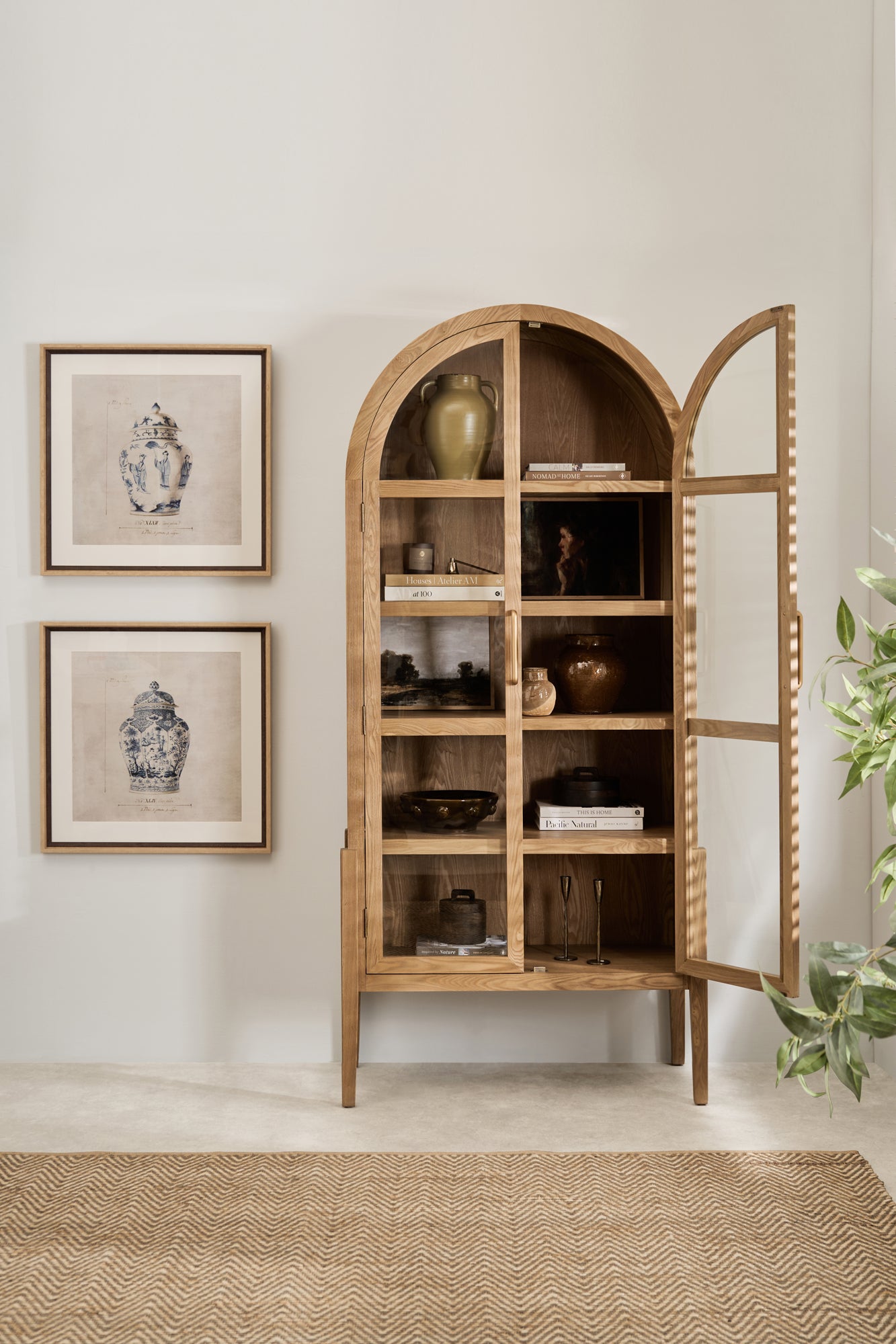Arched natural elm wood display cabinet with glass doors and five interior shelves, styled with ceramic vases and books in a modern living space