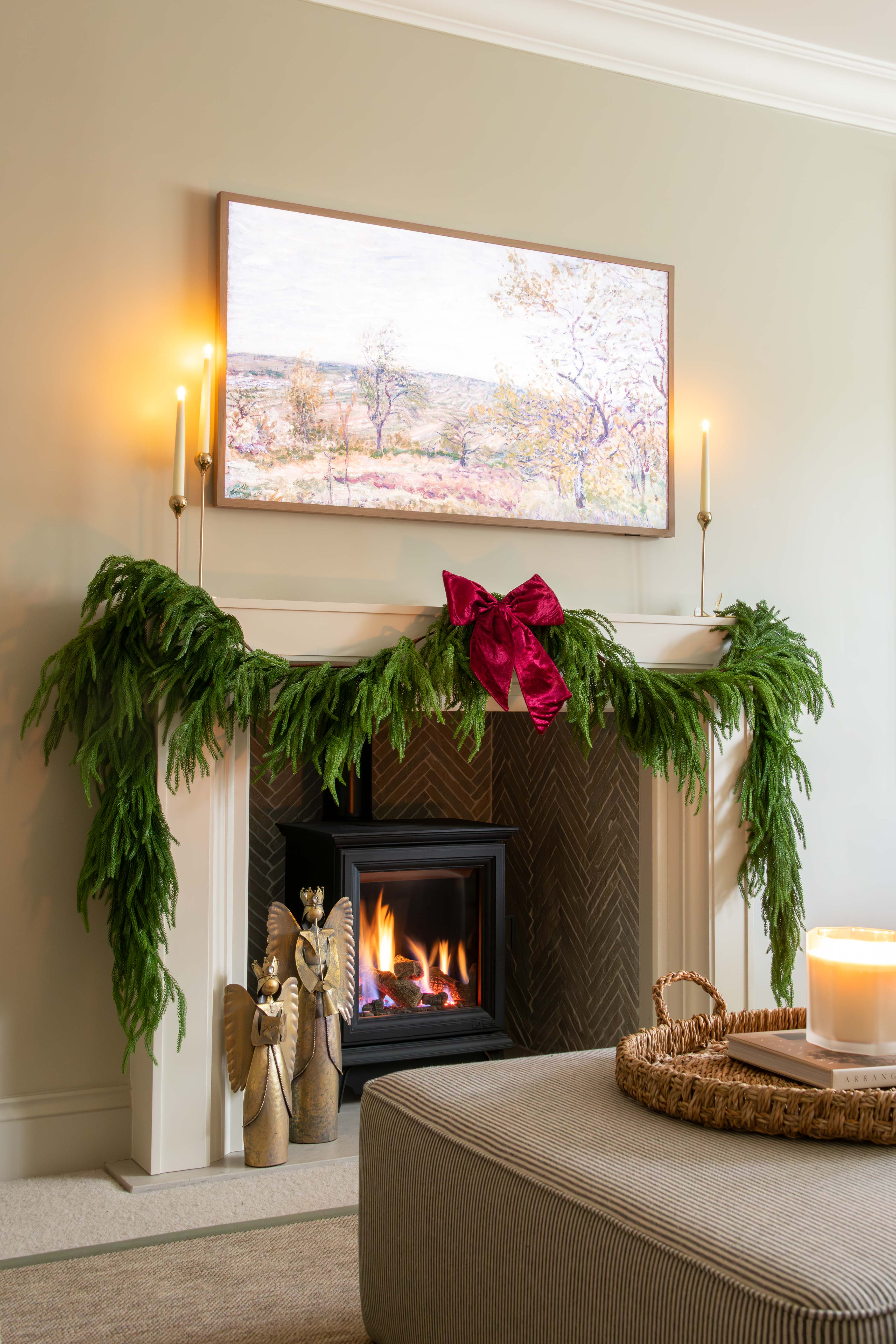 Decorated fireplace with greenery and a candle, framed artwork above, and a cozy living room setting.