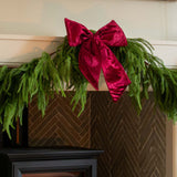 Green garland with a red velvet bow on a fireplace mantel.