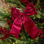 burgundy velvet bow on a decorated Christmas tree with lights and red berries.