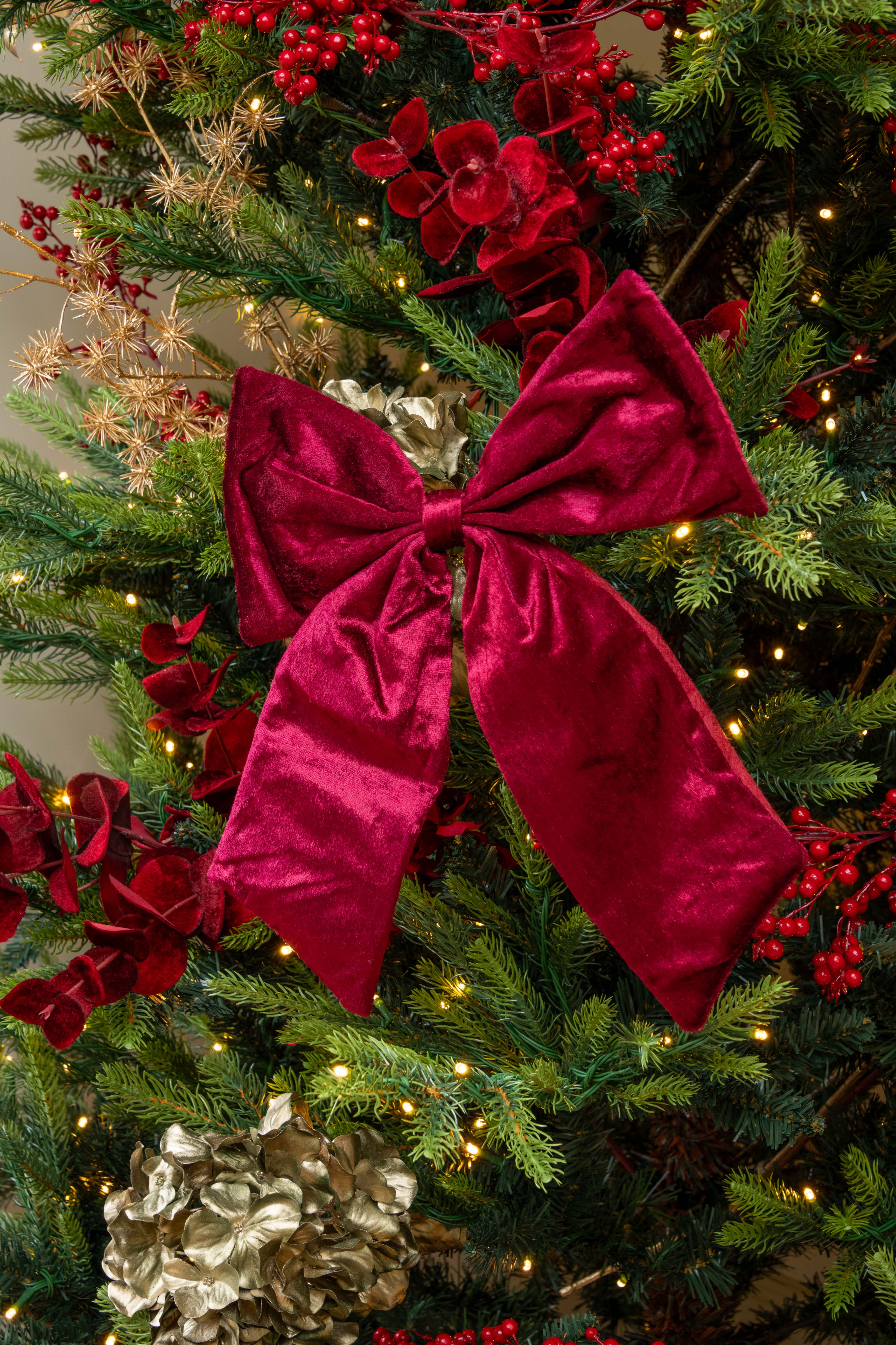 burgundy velvet bow on a decorated Christmas tree with lights and red berries.