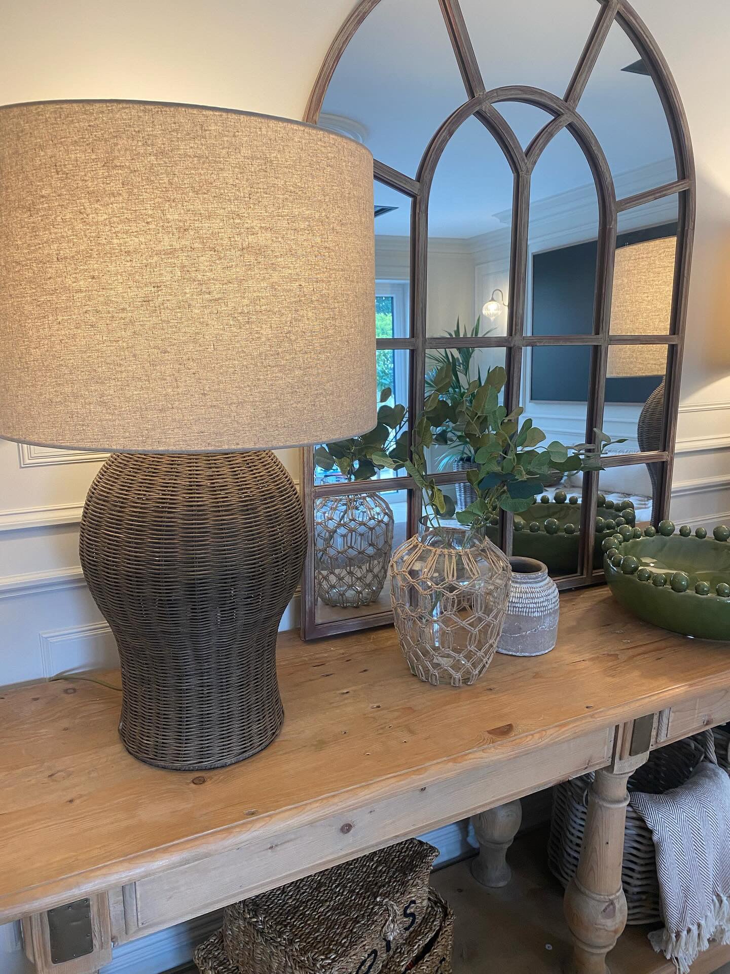 Large rattan lamp with linen shade mirrorsitting on a console table next to a