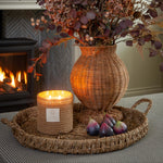 Decorative arrangement with a wicker vase, candle, and figs on a tray in a cozy room.