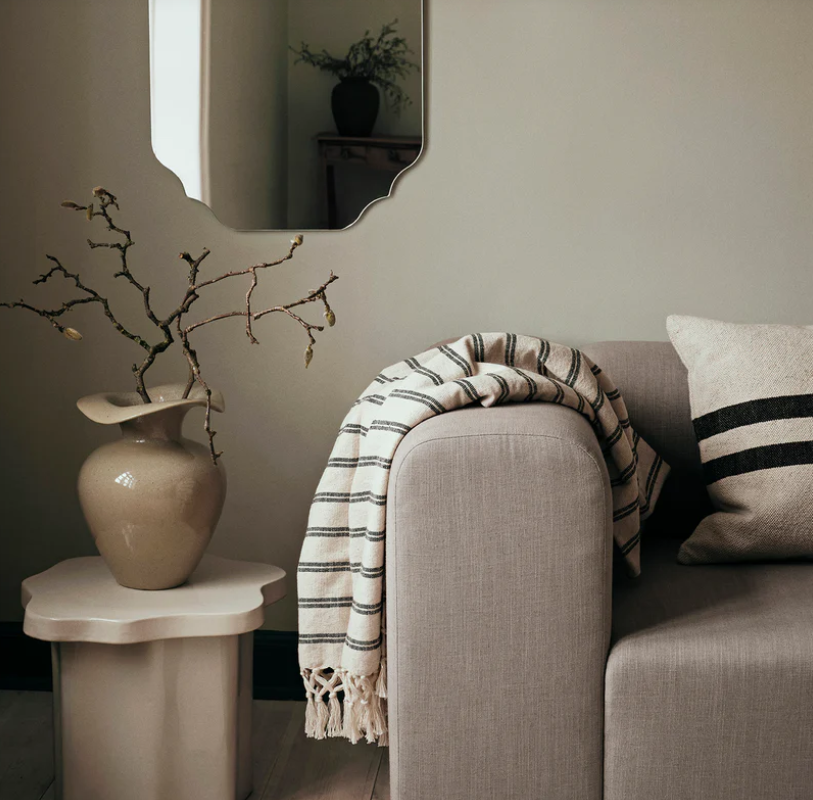 Grey sofa with a striped blanket and pillow, next to a small table with a vase and branches.