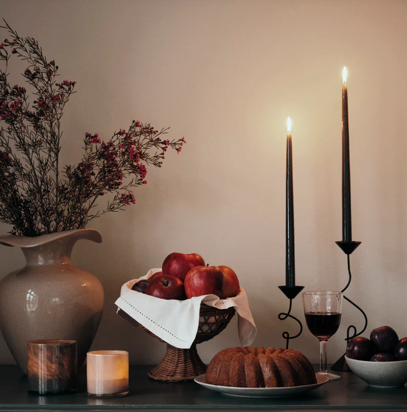 Decorative setting with candles, fruit, and a cake on a table.