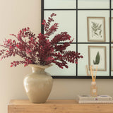 Decorative vase with red flowers on a wooden dresser against a wall with framed pictures.