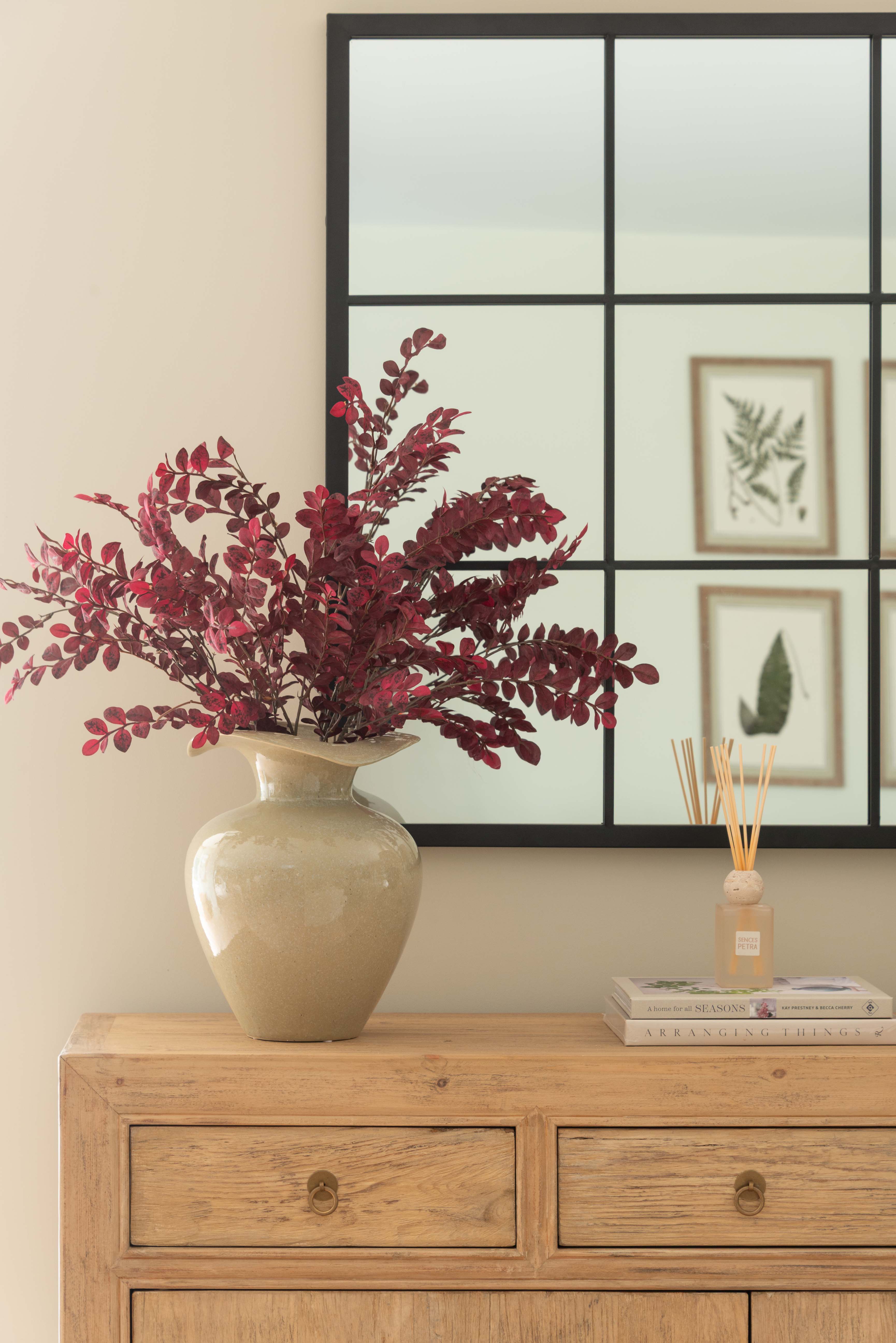 Decorative vase with red flowers on a wooden dresser against a wall with framed pictures.