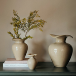 Three beige ceramic vases with a plant on a neutral background