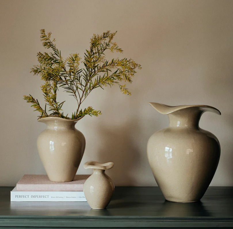 Three beige ceramic vases with a plant on a neutral background
