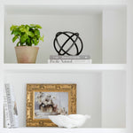 Black metal ring orb decor sculpture on a white shelf beside books and a plant