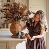 Woman arranging Brown Tall Hydrangea Stems with other seasonal foliage in a wicker vase