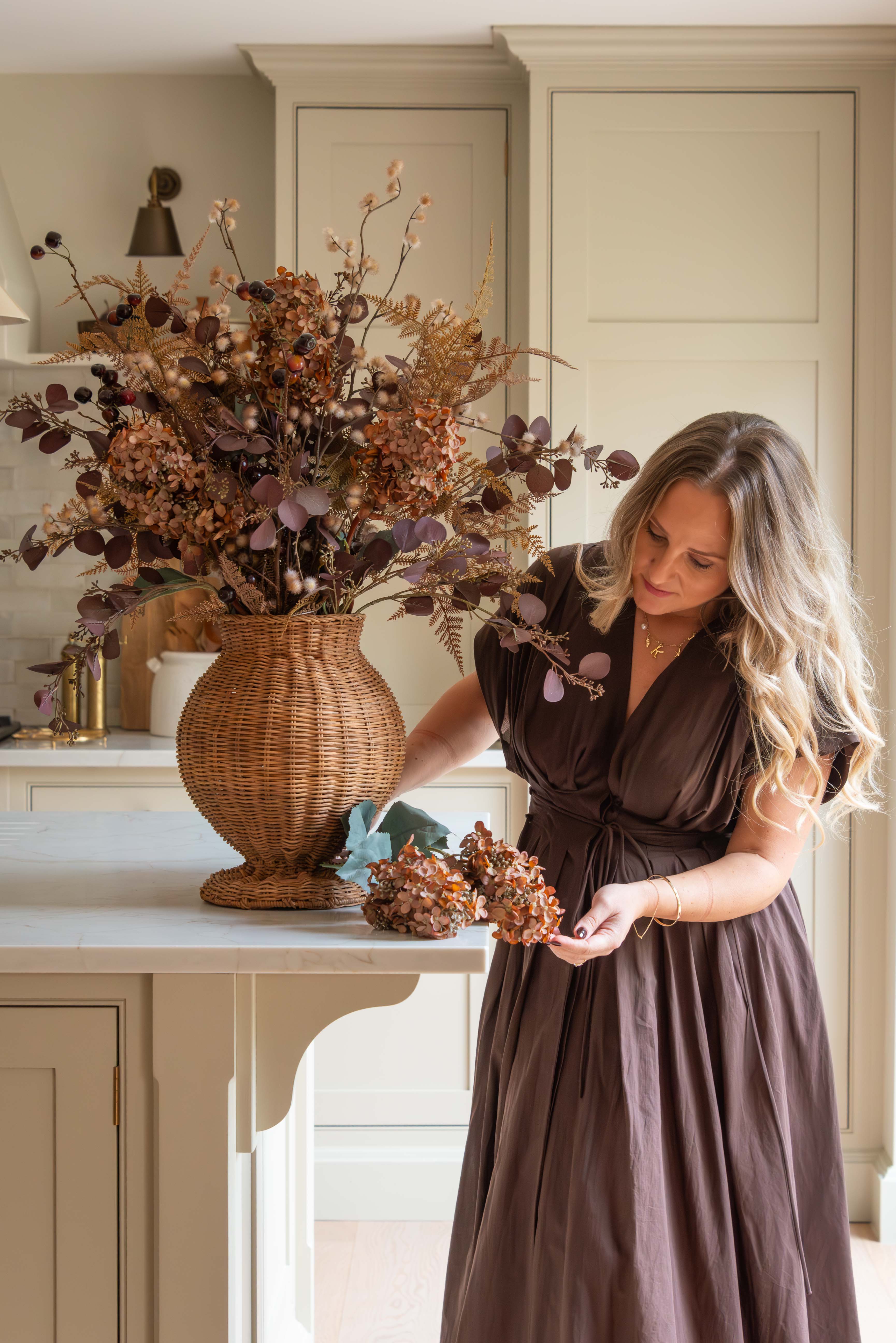 Woman arranging Brown Tall Hydrangea Stems with other seasonal foliage in a wicker vase