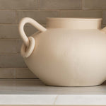 Beige ceramic pot on a kitchen counter with a tiled backsplash