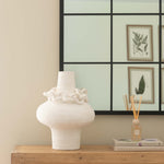 White vase on a wooden dresser with a decorative mirror in the background
