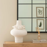 White vase on a wooden dresser with a decorative mirror in the background