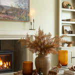 Living room with fireplace, vase of dried ferns, and decorative items.