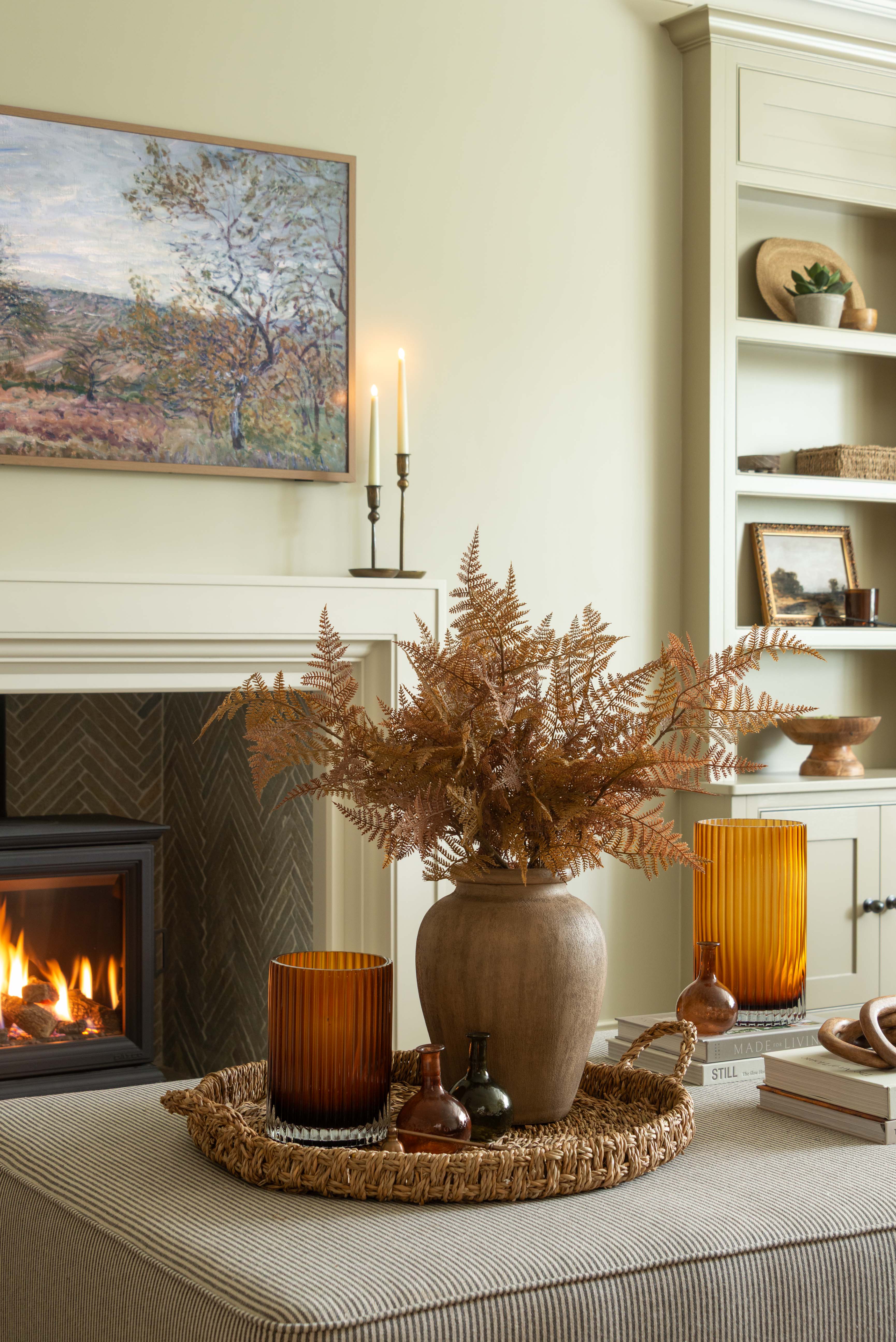 Living room with fireplace, vase of dried ferns, and decorative items.