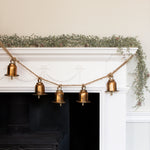 Charles Ted Bell Garland with rustic metal bells hanging on a jute rope across a white mantel decorated with greenery