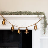 Charles Ted Bell Garland with rustic metal bells hanging on a jute rope across a white mantel decorated with greenery