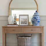 A decorative Chinoiserie pot with lid on a wooden table, alongside a round mirror and other home décor items.