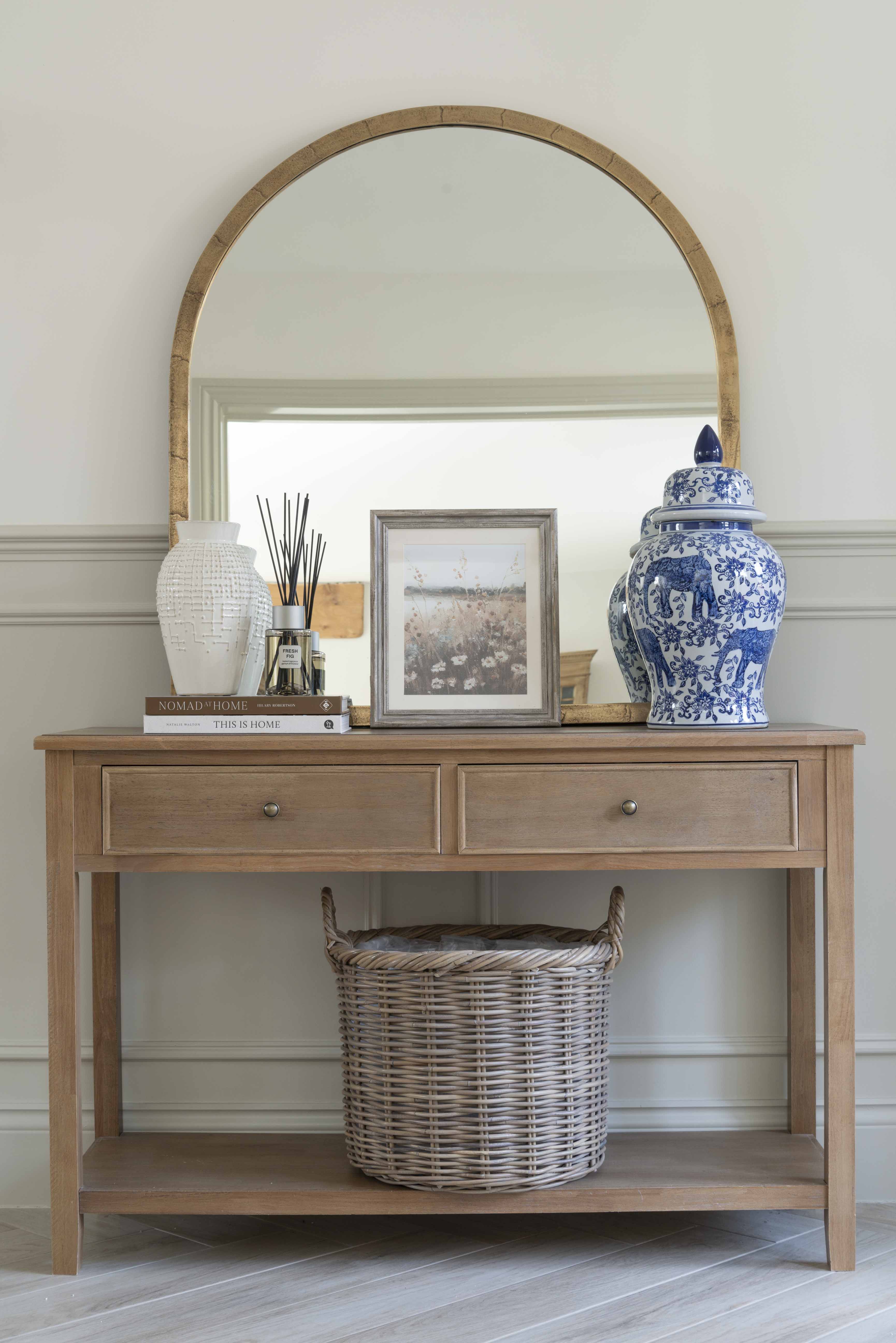 A decorative Chinoiserie pot with lid on a wooden table, alongside a round mirror and other home décor items.