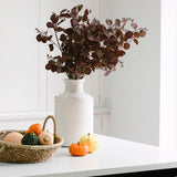 White ceramic vase with a slender bottle-neck design. Filled with autumn florals