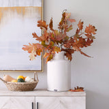 White ceramic bottle vase with autumn leaves styled beside a basket of gourds