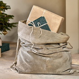 Charles Ted Cotton Velvet Christmas Sack in light grey with gifts inside, styled by a Christmas tree and fireplace