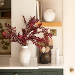 White ceramic vase with red foliage styled on a kitchen counter