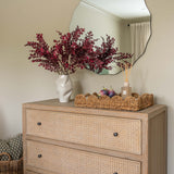 Beige dresser with wicker drawers, decorative flowers, and a mirror on a beige wall.