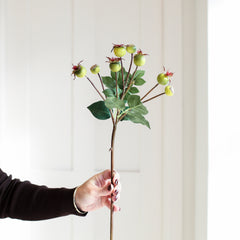 Hand holding a Charles Ted Faux Crab Apple Stem with green apples and leaves against a light background