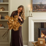 Woman arranging Charles Ted Faux Oak Leaves with Acorns beside a fireplace