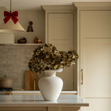Kitchen interior with a vase of flowers on a counter, wooden stools, and neutral color scheme.