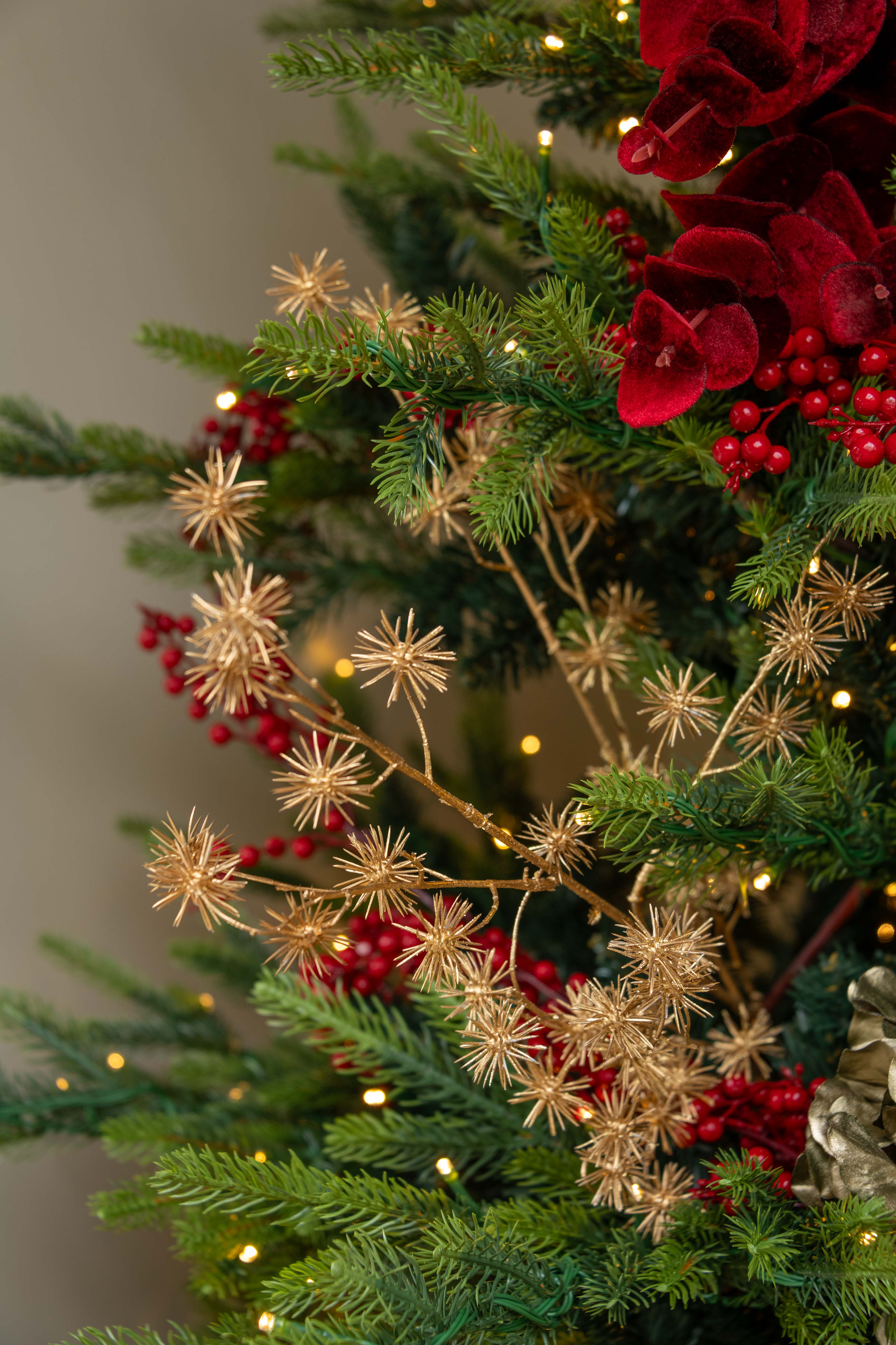 Decorative Christmas tree with red berries and gold branches against a blurred background