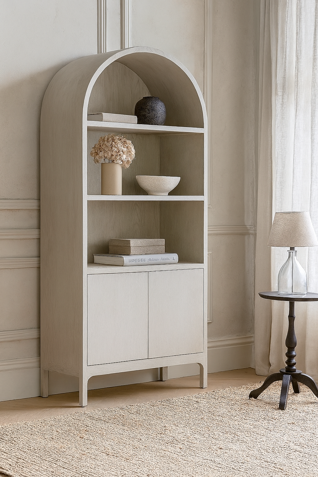 Beige corner bookshelf with decorative items in a room with neutral walls and a lamp.
