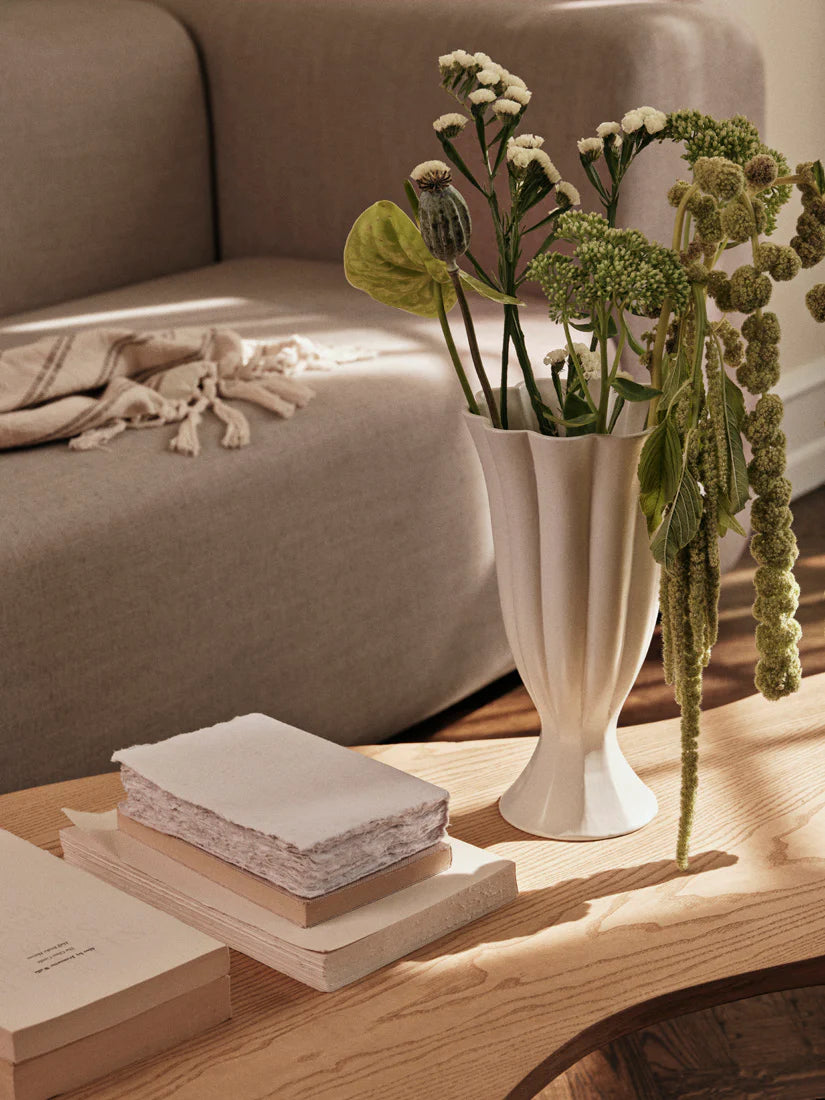 The Ivory Flute Ceramic Vase features a tall, elegant silhouette reminiscent of a blooming tulip. Crafted from high-quality ceramic, its glossy white glaze highlights the fluted vertical ridges that cascade gracefully from the scalloped rim to the flared base. This timeless piece brings a touch of sophistication to any space, whether displayed as a standalone sculpture or filled with fresh florals. Perfect for modern, classic, or minimalist interiors.