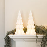 Pair of white lit decorative Christmas trees glowing on a mantelpiece with greenery