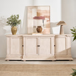 A white oak sideboard with four doors and bronze hardware, placed in a room with decorative items on top and a plant to the side.