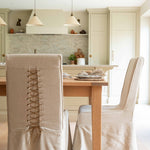 chair features a beautifully tailored loose linen slipcover in a natural beige hue, accented with a charming corset-style lace-up back for added visual interest and secure fit.