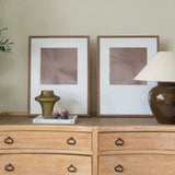 Wooden dresser with two framed pictures and a lamp on top against a beige wall.