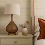 Nighstand with lamp and decorative items next to a bed with orange pillow.