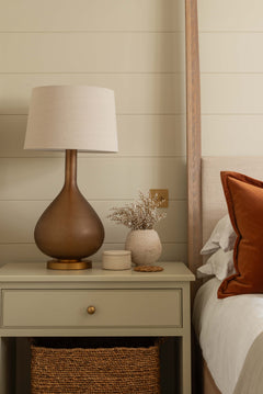 Nighstand with lamp and decorative items next to a bed with orange pillow.