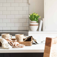Two Charles Ted Organic Natural Mugs styled on a kitchen counter with woven tray and napkins
