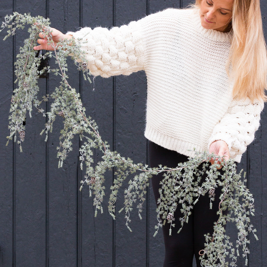 Charles Ted Pine Garland with frosted greenery and pinecones held by woman in a white jumper